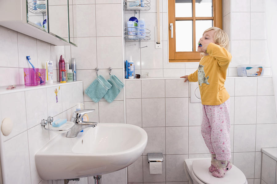 Girl standing on toilet, brushing teeth in bathroom Photograph by Westend61