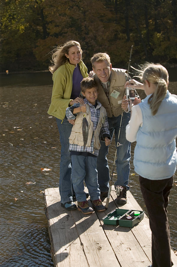 Girl taking photograph of family fishing Photograph by Comstock Images