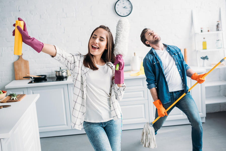Girlfriend And Boyfriend In Rubber Gloves Singing And Playing Mop Like Guitar In Kitchen Photograph by LightFieldStudios