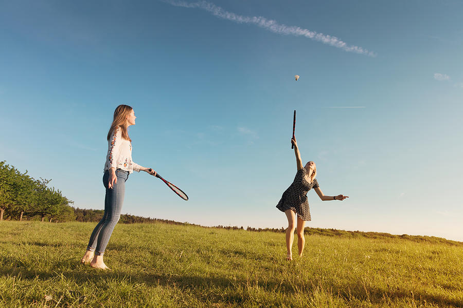 Girlfriends playing badminton on grassy field during sunset Photograph by Kamisoka