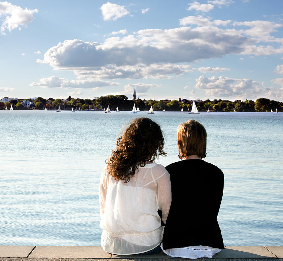 Girlfriends sitting on pier looking out over water Photograph by Deepblue4you