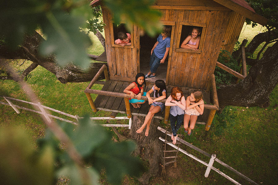 Girls and boys talking and playing in a wooden treehouse Photograph by Wundervisuals