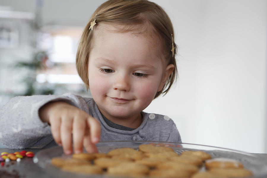 Girls looking down selecting fresh baked cookie smiling Photograph by Judith Haeusler