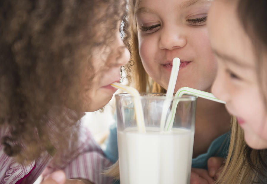 Girls sharing glass of milk Photograph by JGI/Jamie Grill