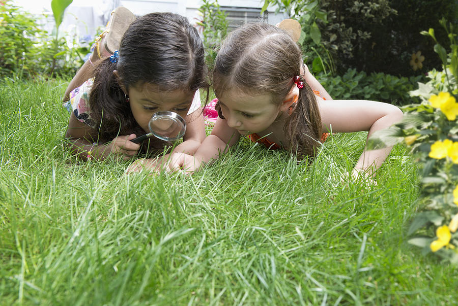 Girls using magnifying glass in grass Photograph by Jose Luis Pelaez Inc