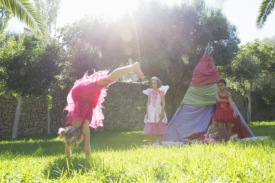 Girls watching friend in fairy costume doing handstand in garden Photograph by Russ Rohde