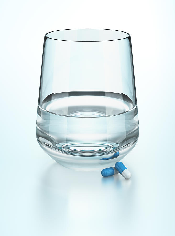 Glass of water with two medication capsules Photograph by Atomic Imagery