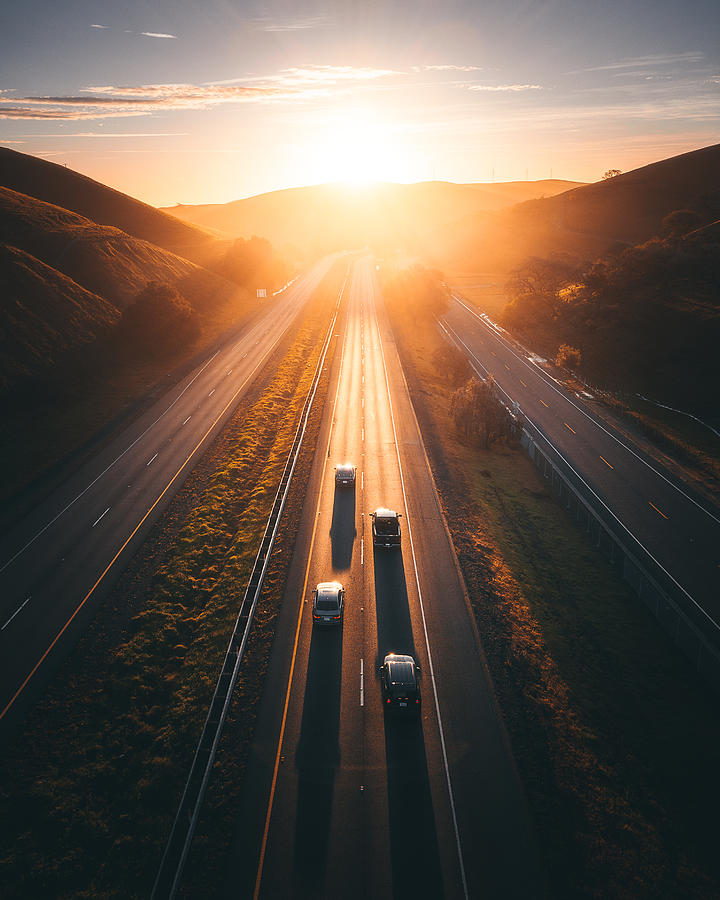 Golden light illuminates a remote highway with four cars on it Photograph by Andrew Wille