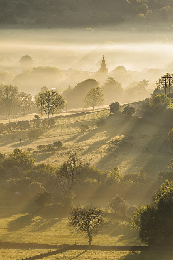 Golden sunrays through the mist with the Parish church of St Peter, Hope village. English Peak District. UK. Photograph by John Finney Photography