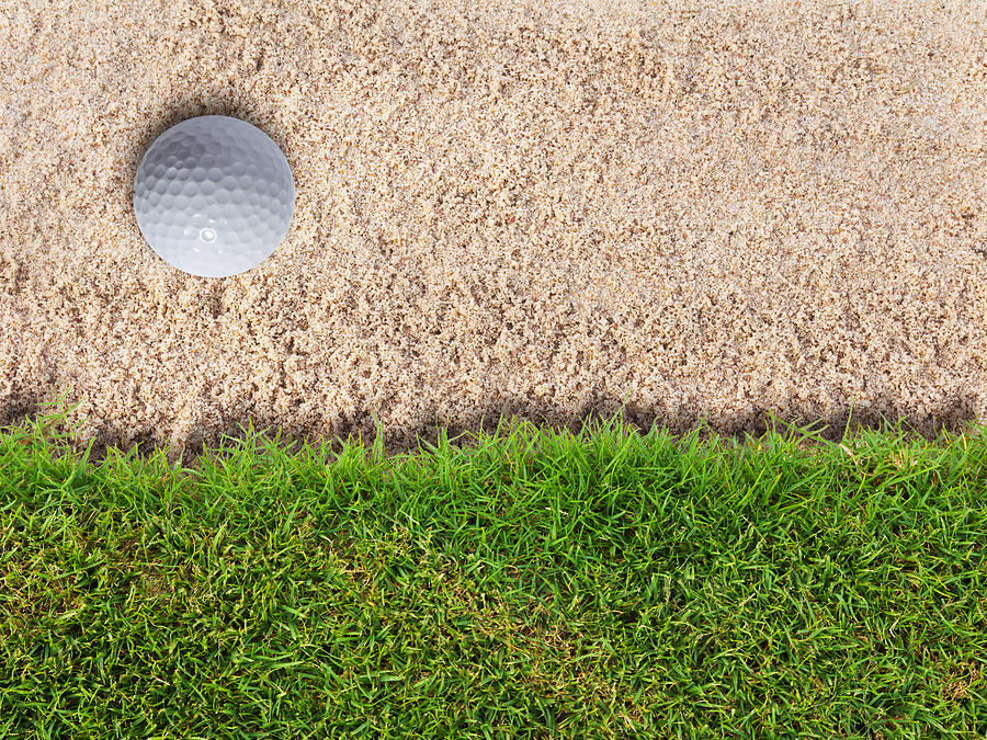 Golf ball in sand bunker near fresh green grass Photograph by Luckpics