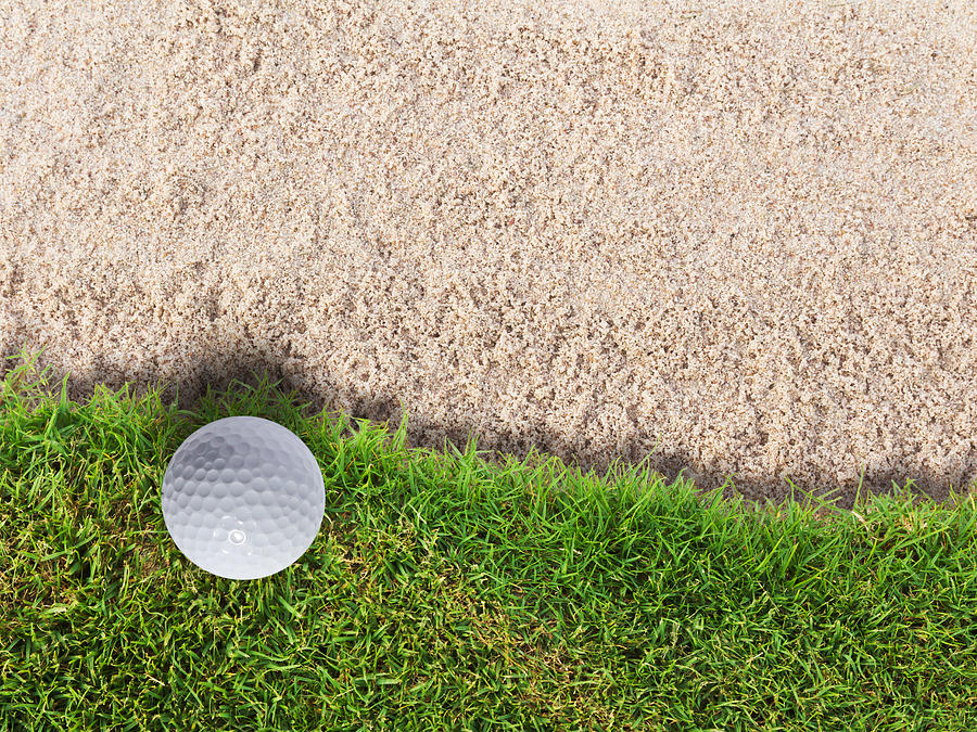 Golf ball on green grass near sand bunker Photograph by Luckpics