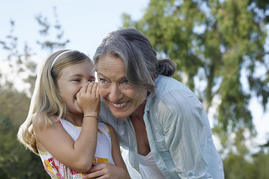 Granddaughter (5-6) whispering to grandmothers ear outdoors Photograph by Moodboard