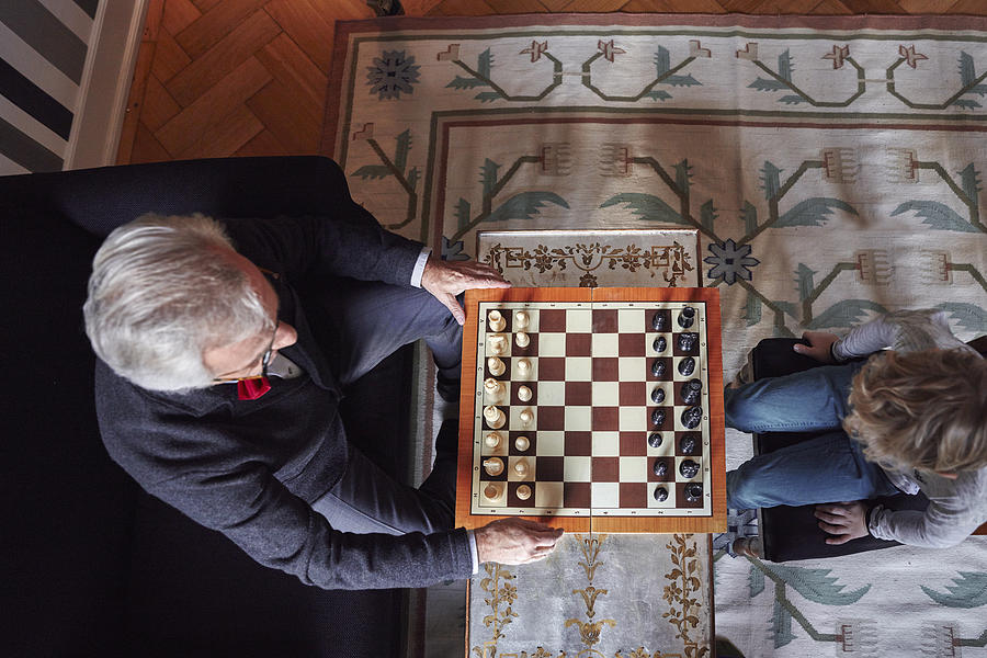 Grandfather and grandson playing chess in living room Photograph by Westend61