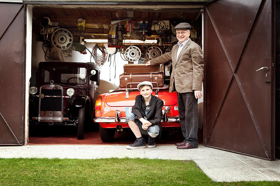 Grandfather and grandson with vintage car and trunk suitcases in garage Photograph by Image Source