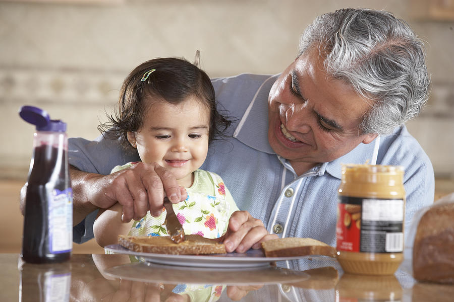 Grandfather helping granddaughter (12-15 months) make sandwich Photograph by SW Productions