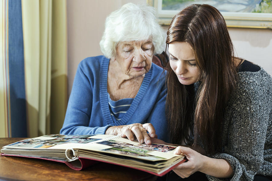 Grandmother and granddaughter looking at photo album in house Photograph by Maskot