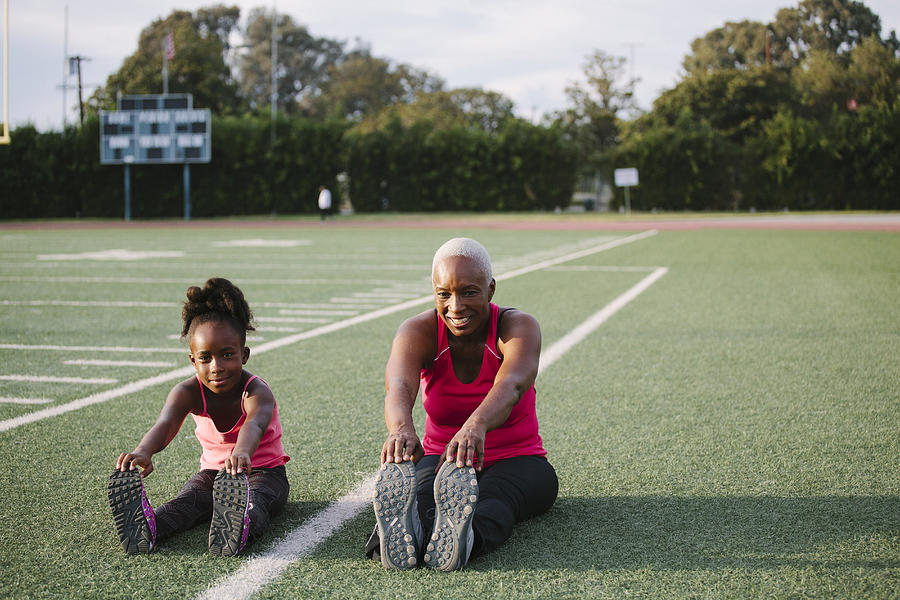 Grandmother and granddaughter stretching on football field Photograph by Shestock