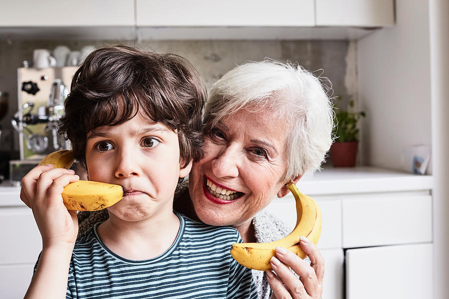 Grandmother and grandson fooling around, using bananas as telephones, laughing Photograph by Emely