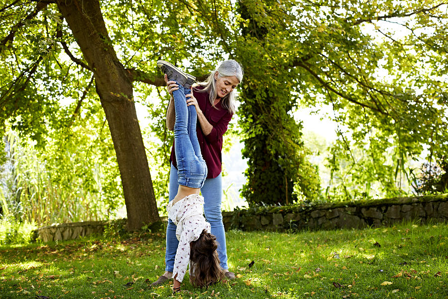 Grandmother assisting girl in doing handstand Photograph by Morsa Images