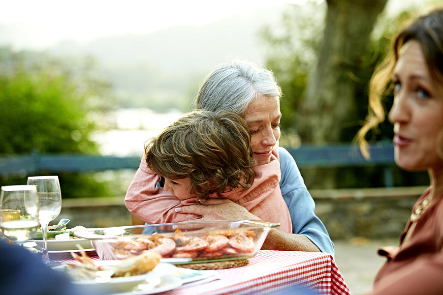 Grandmother embracing grandson at outdoor table Photograph by Morsa Images