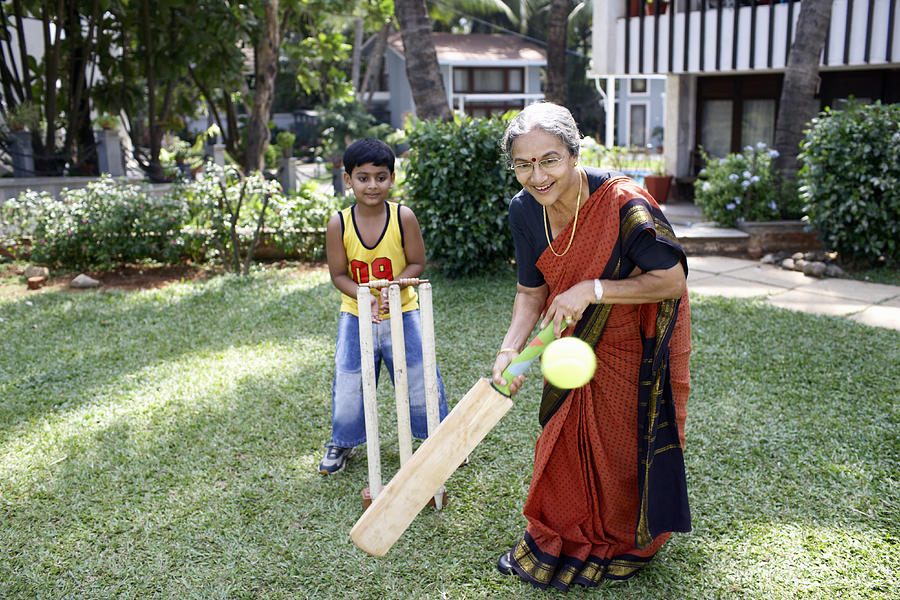 Grandmother playing cricket with grandson (6-8) batting ball, smiling Photograph by Karan Kapoor
