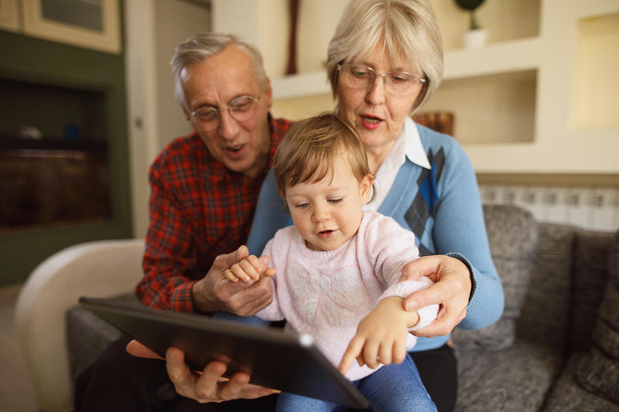 Grandparents and grandchild using digital tablet at home Photograph by EmirMemedovski