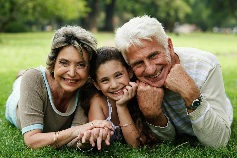 Grandparents and granddaughter (8-10) lying on grass, smiling Photograph by Maria Teijeiro