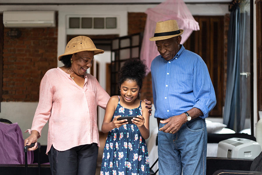 Grandparents and granddaughter using mobile phone in the room Photograph by FG Trade