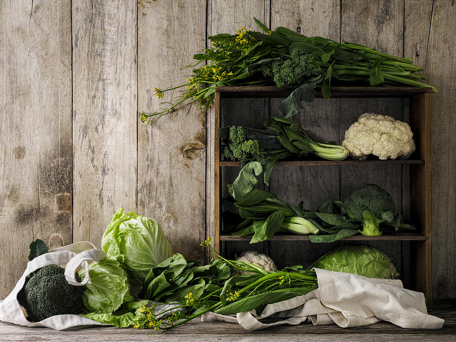 Green leafy vegetables on old rustic wooden shelves and an old weathered table against an old weathered wood plank wall background. Photograph by Enviromantic