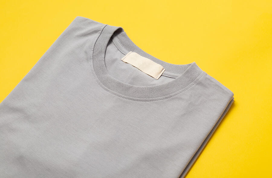 Grey folded t-shirt with blank tag for your design isolated on yellow background Photograph by Thatphichai Yodsri