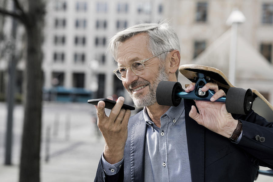 Grey-haired businessman with longboard and smartphone Photograph by Westend61