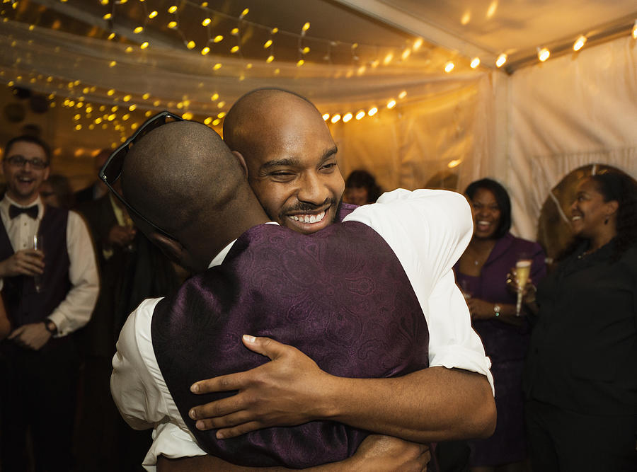 Groom hugging groomsman at reception Photograph by Roberto Westbrook