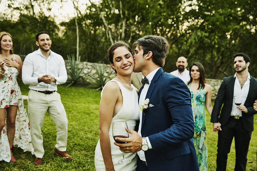 Groom kissing bride on cheek during wedding reception at tropical resort Photograph by Thomas Barwick