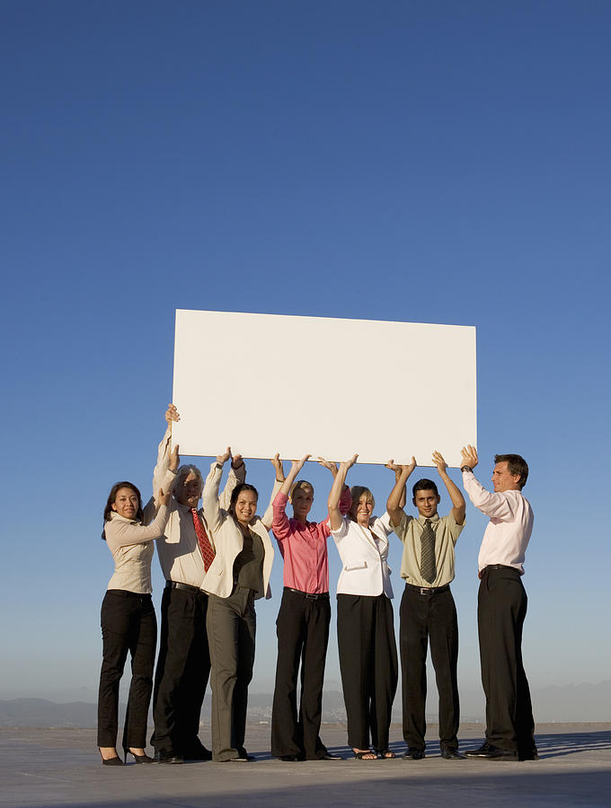Group of business people holding a blank board on roof Photograph by Nick Dolding