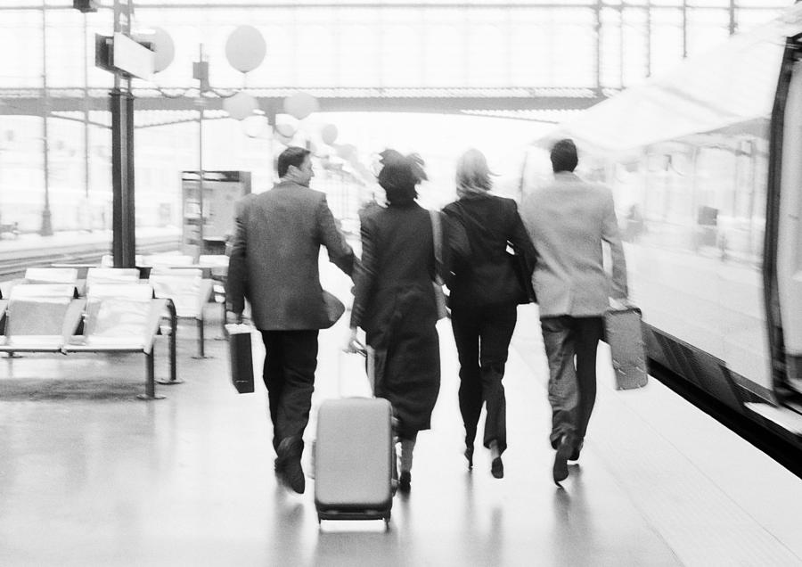 Group of business people walking next to train in station, rear view, b&w. Photograph by Teo Lannie