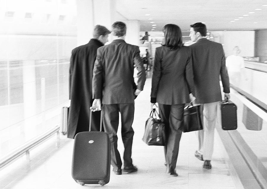 Group of business people walking through terminal, full length, rear view, b&w. Photograph by Teo Lannie