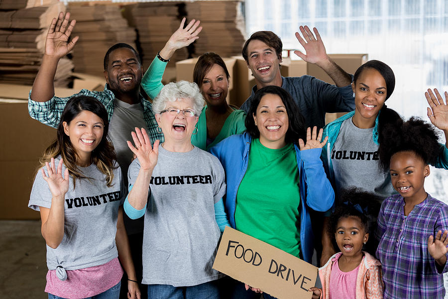 Group of cheerful volunteers waving during food drive Photograph by SDI Productions