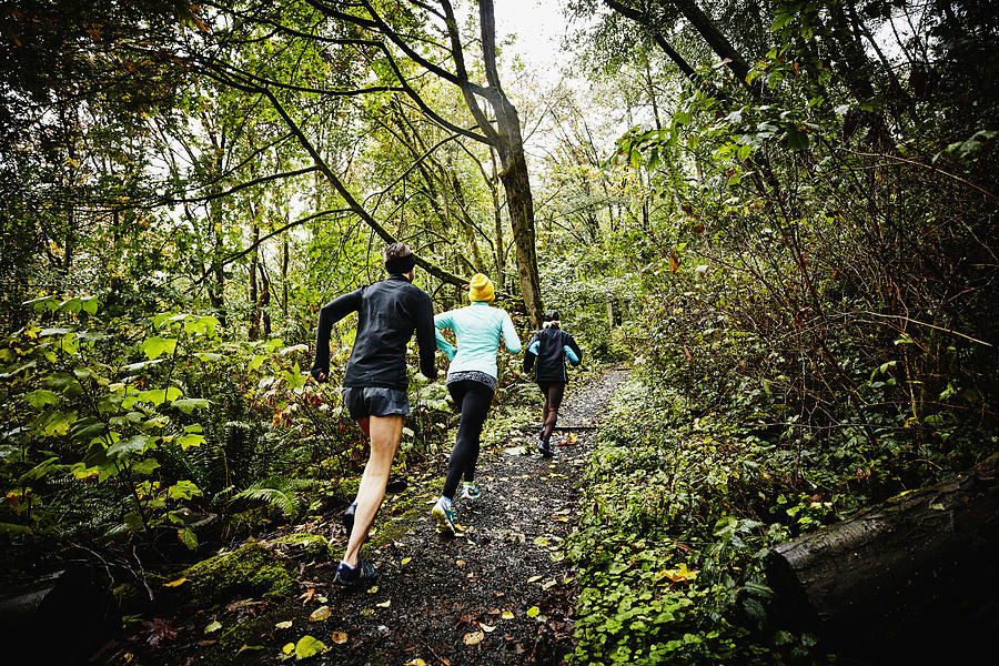 Group of female friends running up forest trail Photograph by Thomas Barwick
