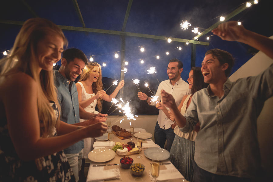 Group of friends holding sparklers and sharing a meal and a drink of champagne outdoors Photograph by Courtneyk
