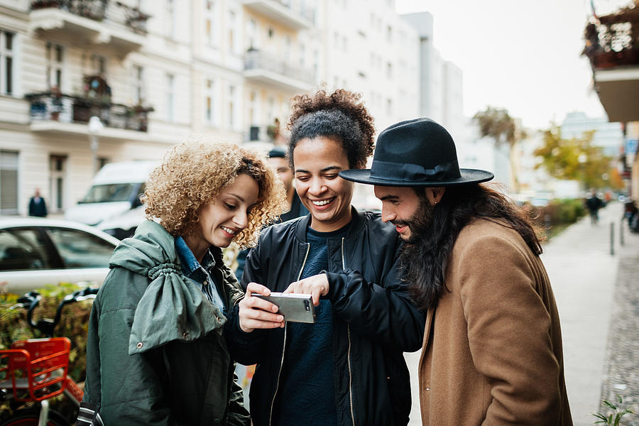 Group Of Friends Looking At Smartphone In Street Photograph by Hinterhaus Productions
