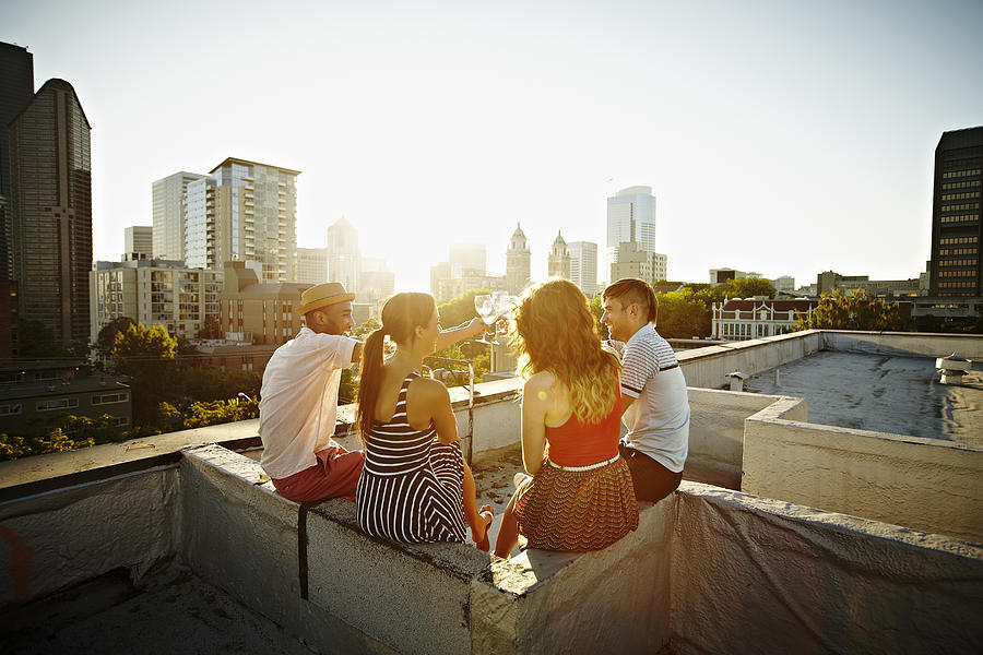 Group of friends on roof toasting at sunset Photograph by Thomas Barwick