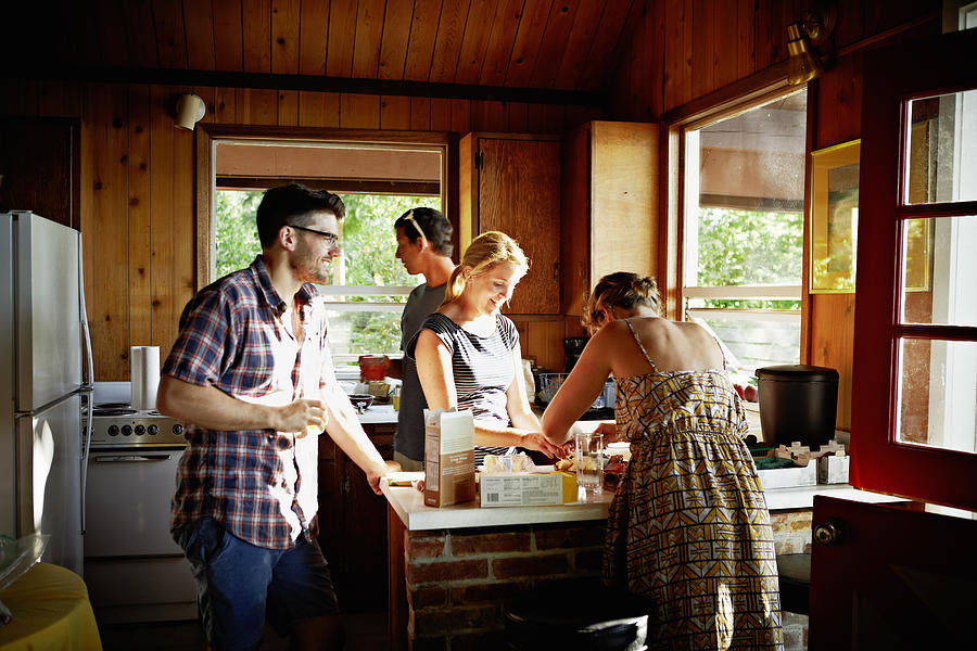 Group of friends preparing a meal in rustic cabin Photograph by Thomas Barwick