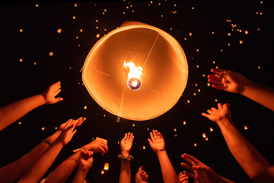 group of hands together releasing the flying lantern with numerous lanterns in the sky, yeepeng festival , Chiangmai, Thailand Photograph by ImpossiAble