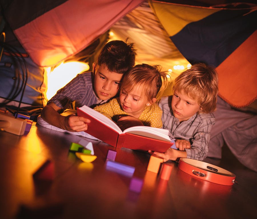Group of kids under blanket fort reading a story together Photograph by Wundervisuals