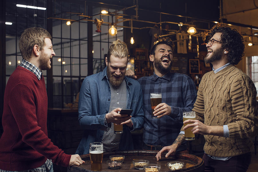Group of Men Having a Laugh at the Pub While Drinking Beer and Watching a Football Game on the Mobile Phone Photograph by FreshSplash