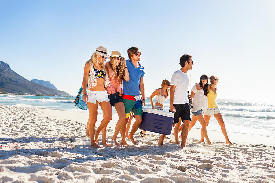 Group of people carrying cooler to party on beach Photograph by Wundervisuals