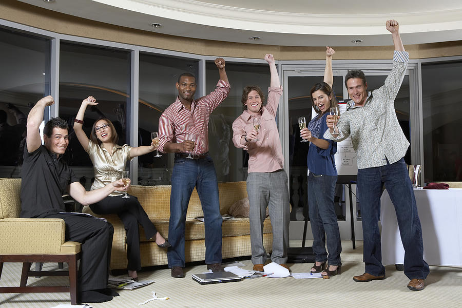 Group of people celebrating in hotel room, arms up, cheering, portrait Photograph by Chris Clinton