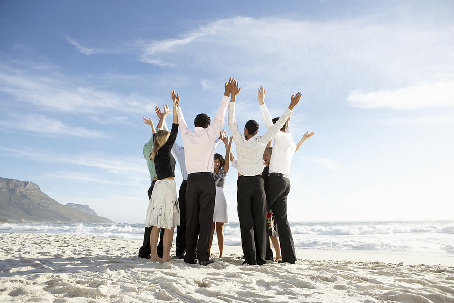 Group of people standing in circle on beach, arms raised Photograph by Plustwentyseven