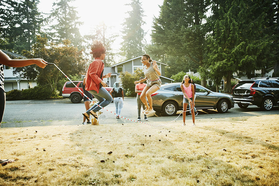 Group of teenage friends jumping rope together in front yard on summer evening Photograph by Thomas Barwick