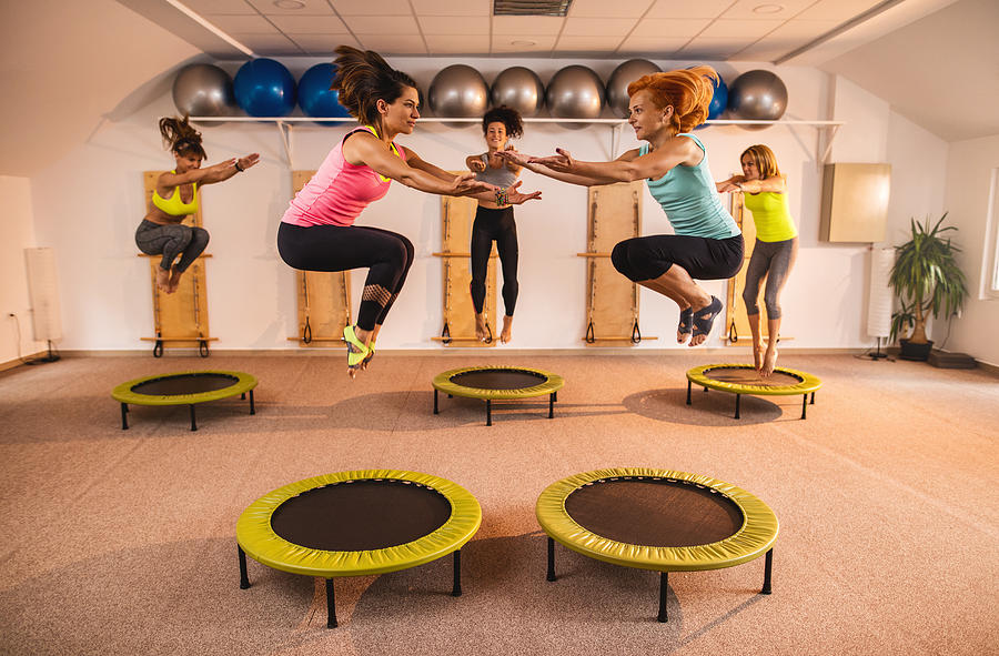 Group of women jumping on trampolines during Pilates exercise class. Photograph by Skynesher